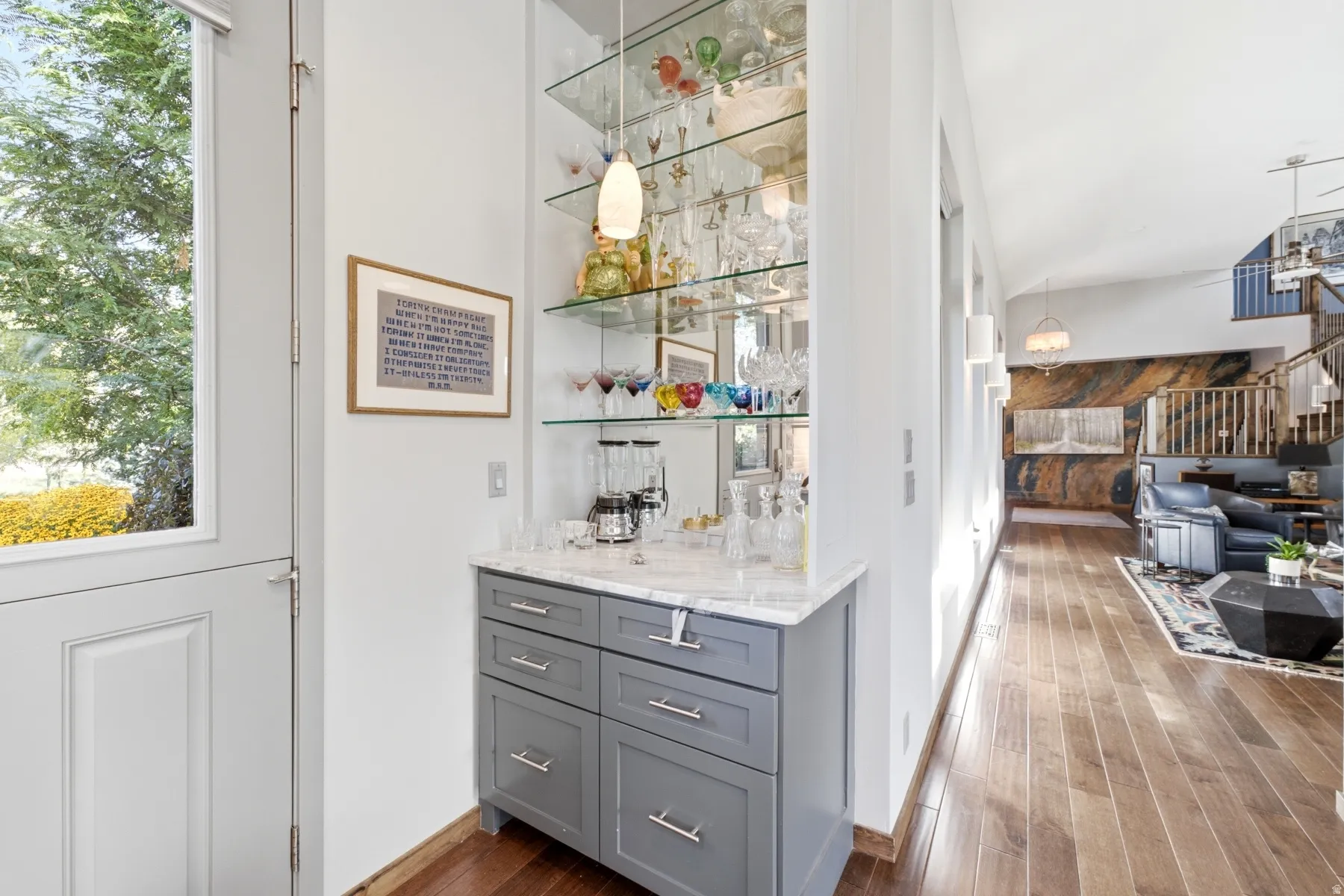 Built-in bar with glass shelving and integrated lighting, gray cabinetry, and a stone countertop