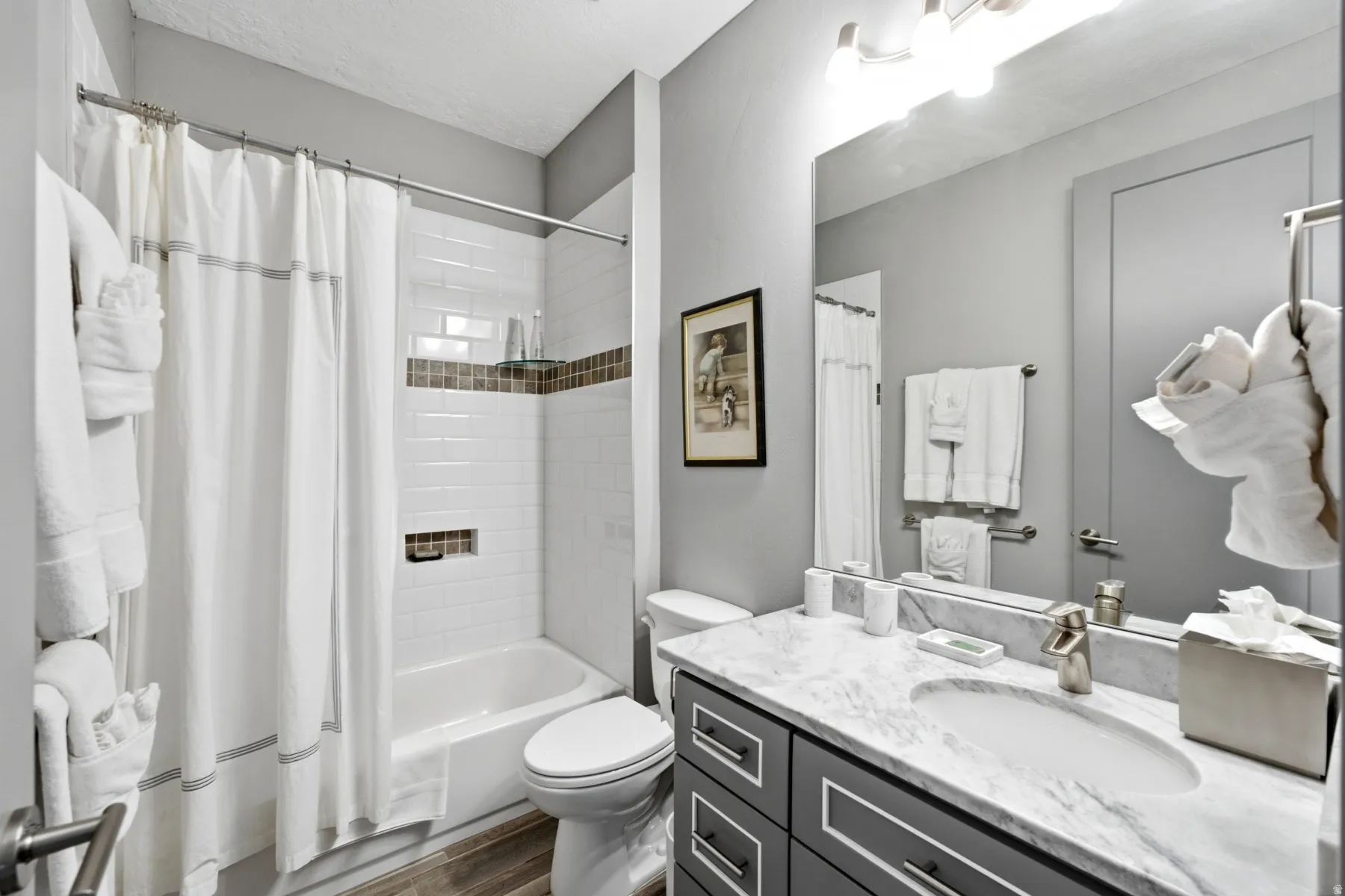 Bathroom featuring a built-in tub with a white subway tile surround, integrated shower niches, a vanity with a white countertop and undermount sink, and a large wall mirror