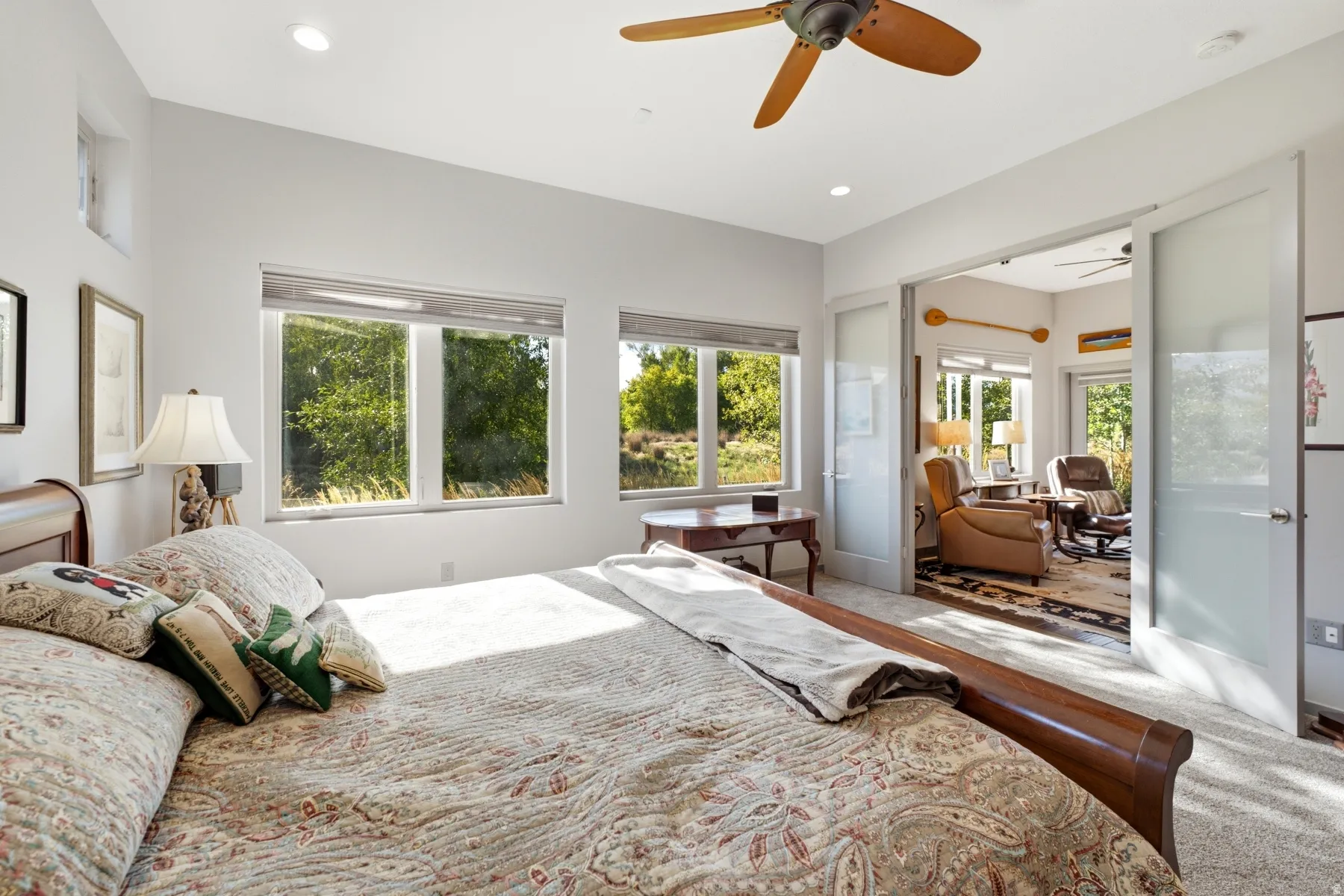 Recessed lighting, wood-finish ceiling fan, multiple windows with roller blinds, carpeted flooring, and sliding frosted glass doors