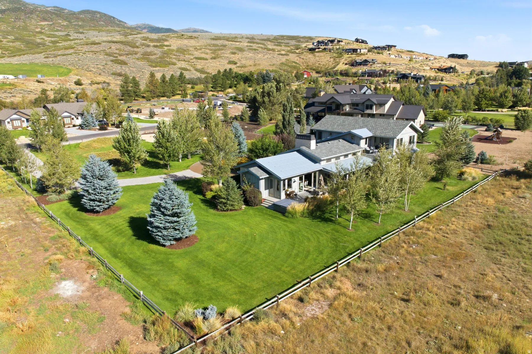 Expansive green lawn with mature evergreen trees, modern exterior with a metal roof, and surrounding natural landscape