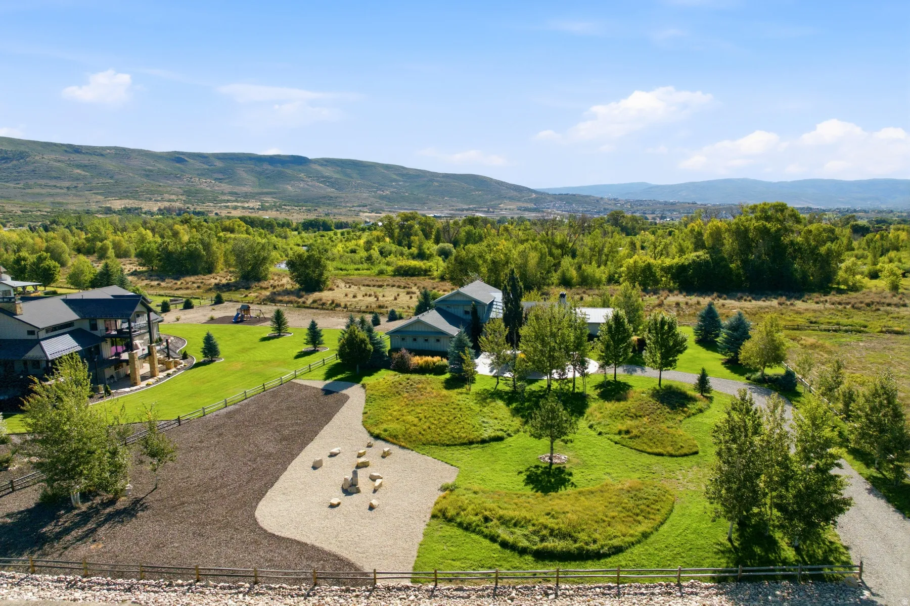 Expansive property featuring a gravel driveway, landscaped grounds with mature trees, and a distant mountain backdrop