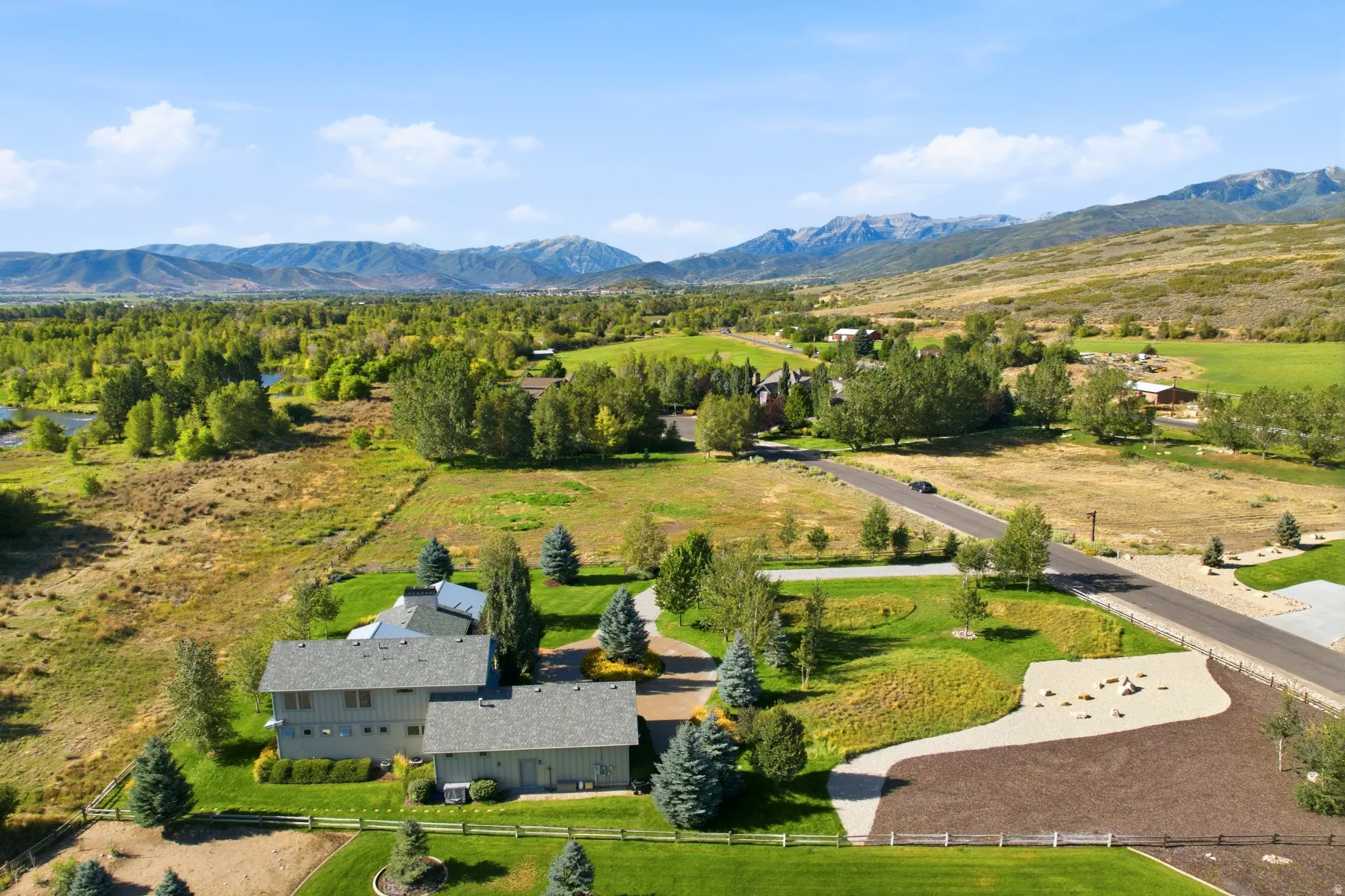 Expansive property featuring a multi-level residence, detached garage structure, paved driveway, and manicured lawns, all set against a backdrop of distant mountains