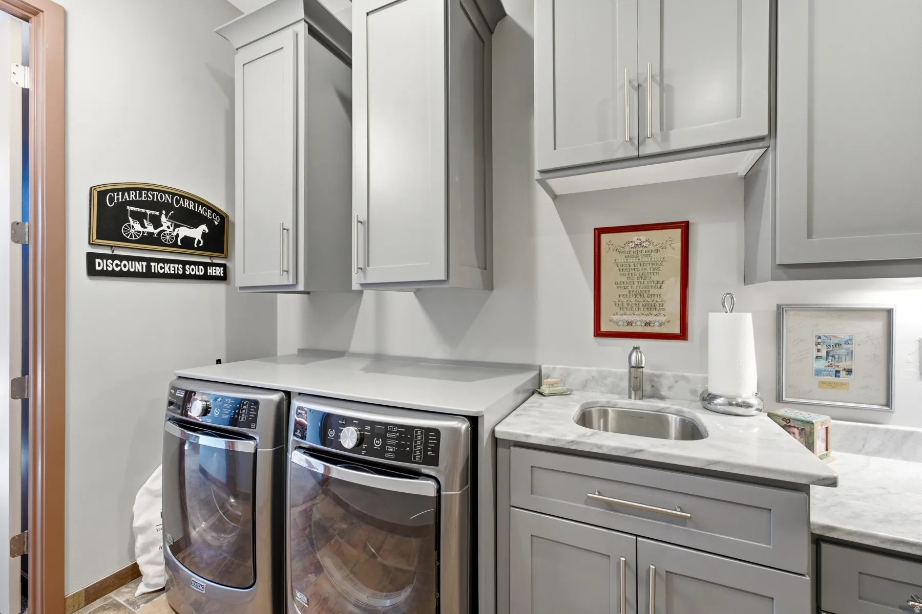 Integrated laundry area featuring light gray cabinetry, stainless steel sink, light-toned countertop, and dual front-load appliances