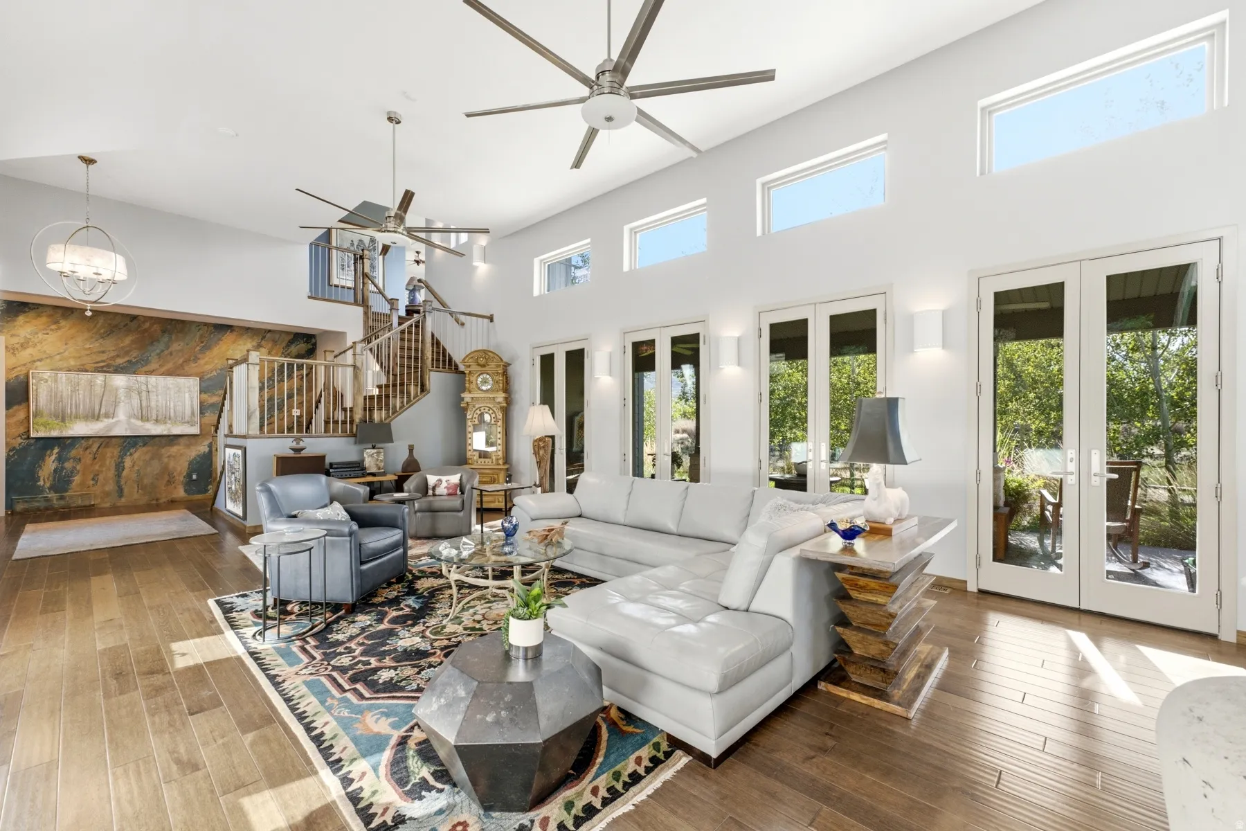 Vaulted ceilings with contemporary ceiling fans, wood-finish flooring, multiple sets of glass-paned French doors, a prominent staircase with wood railing, and a feature wall with stone-finish paneling
