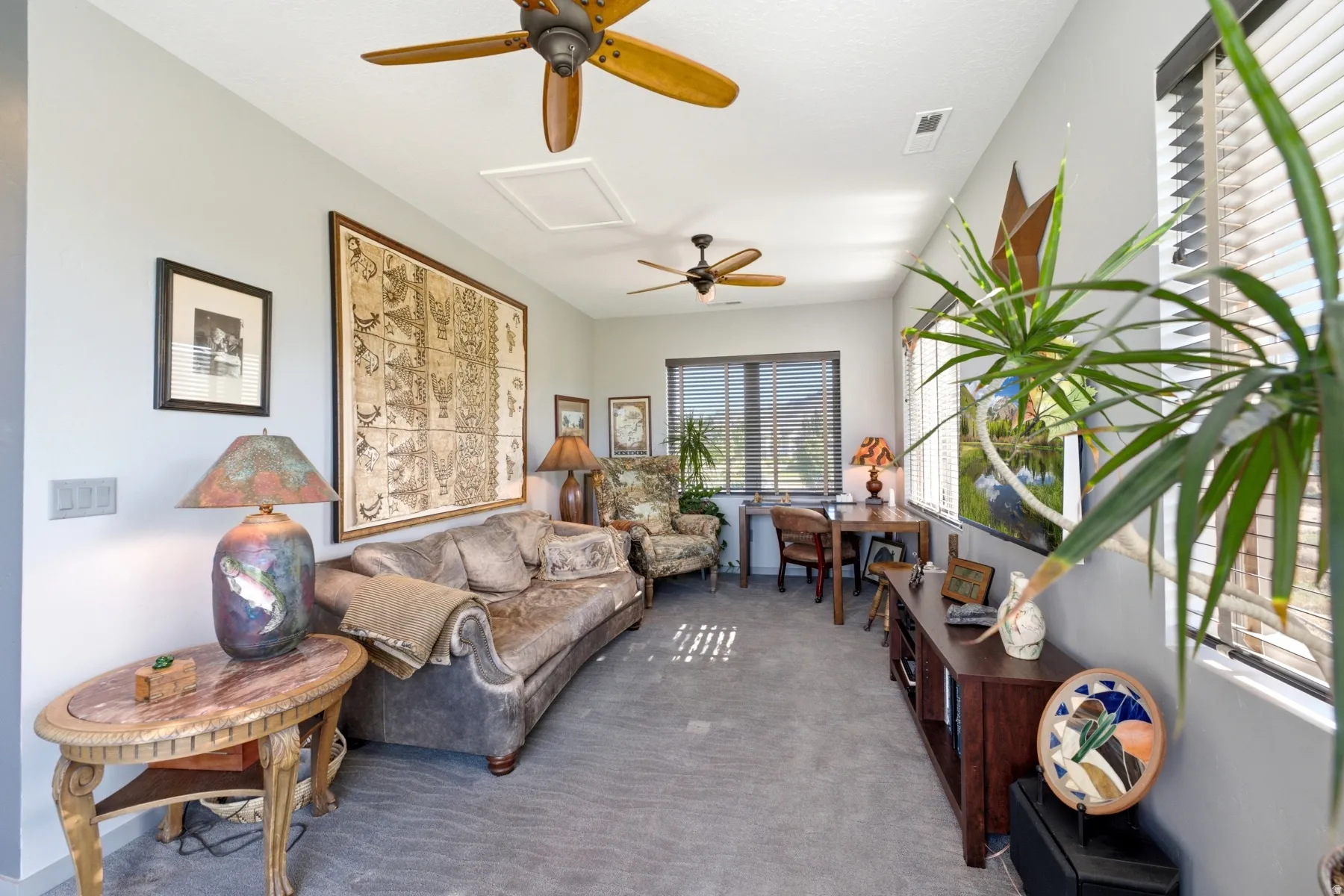 Two ceiling fans with wood-finish blades, multiple windows with horizontal blinds, and light gray wall paint