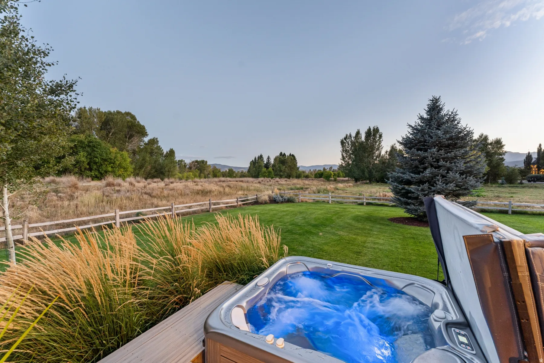 Outdoor spa with integrated lighting, surrounded by a manicured lawn and mature landscaping