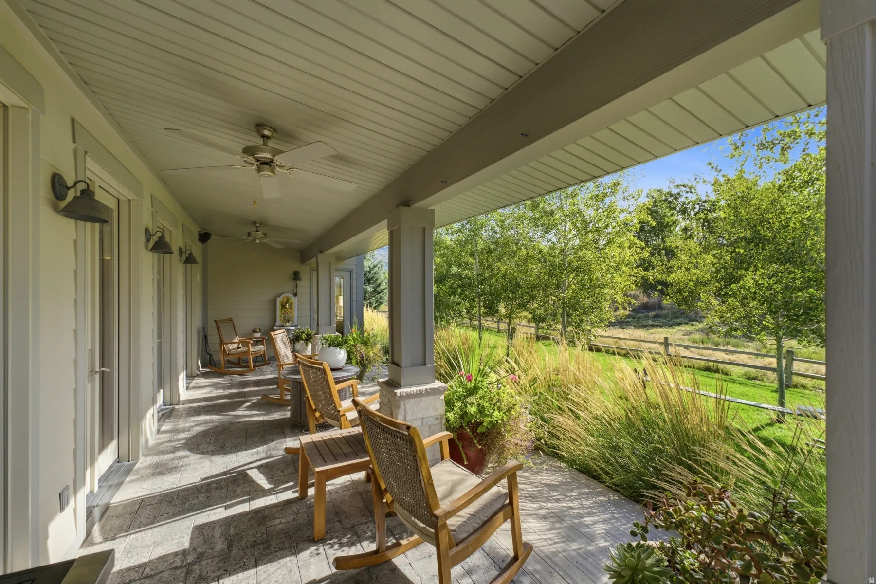 Covered porch featuring stamped concrete flooring, multiple ceiling fans, and sconce lighting