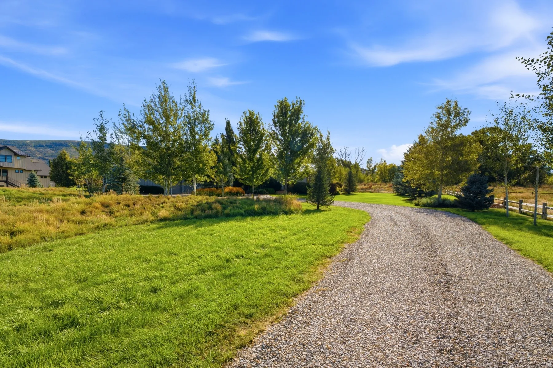 Expansive gravel driveway leading to the property, surrounded by mature trees and manicured lawn