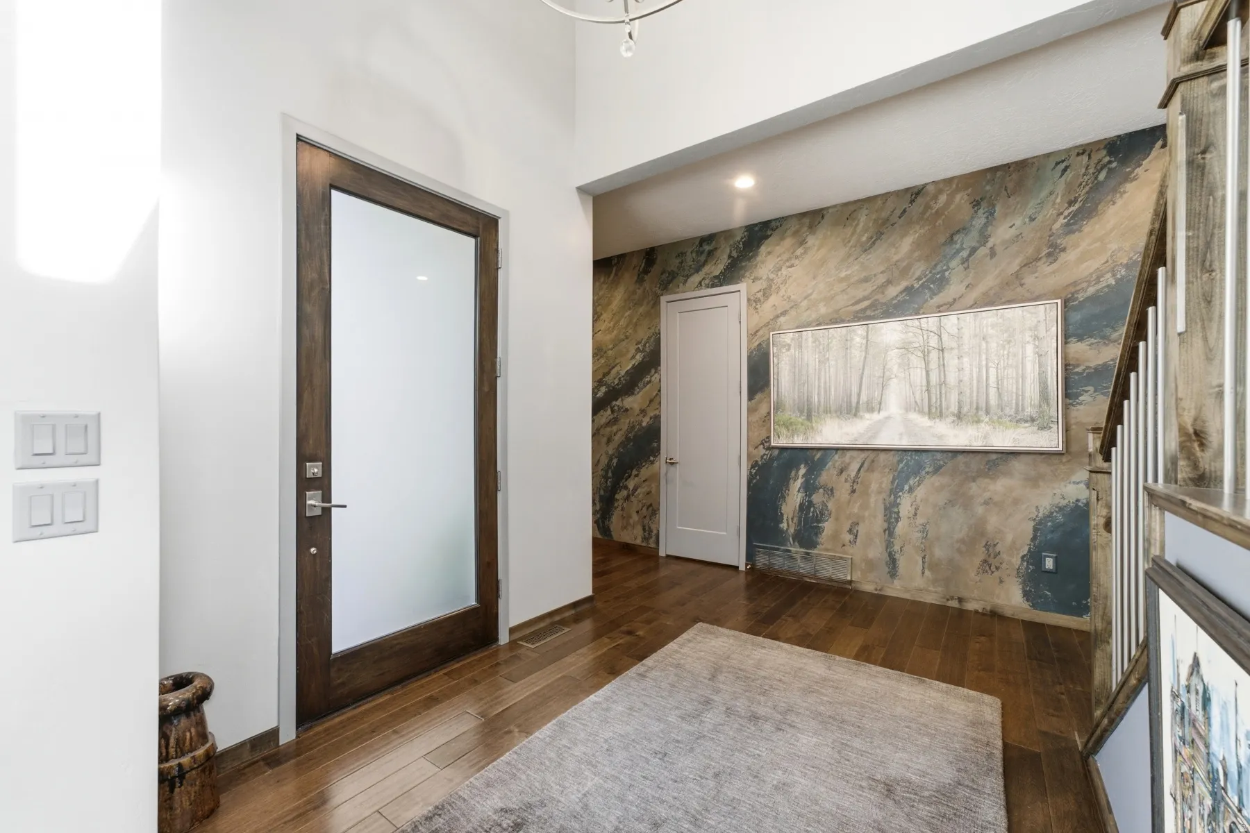 Hardwood flooring throughout the entry, frosted glass panel entry door, and a textured accent wall