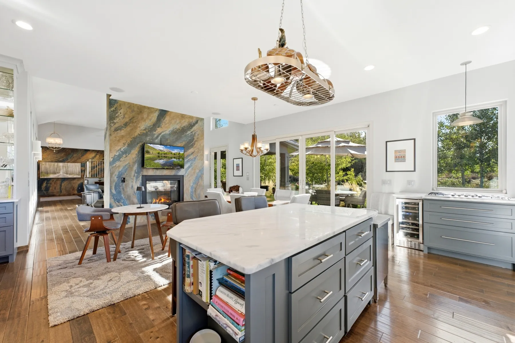 Open-concept interior featuring wood-finish flooring, a kitchen island with stone countertop, stainless steel appliances, and a fireplace with a textured surround