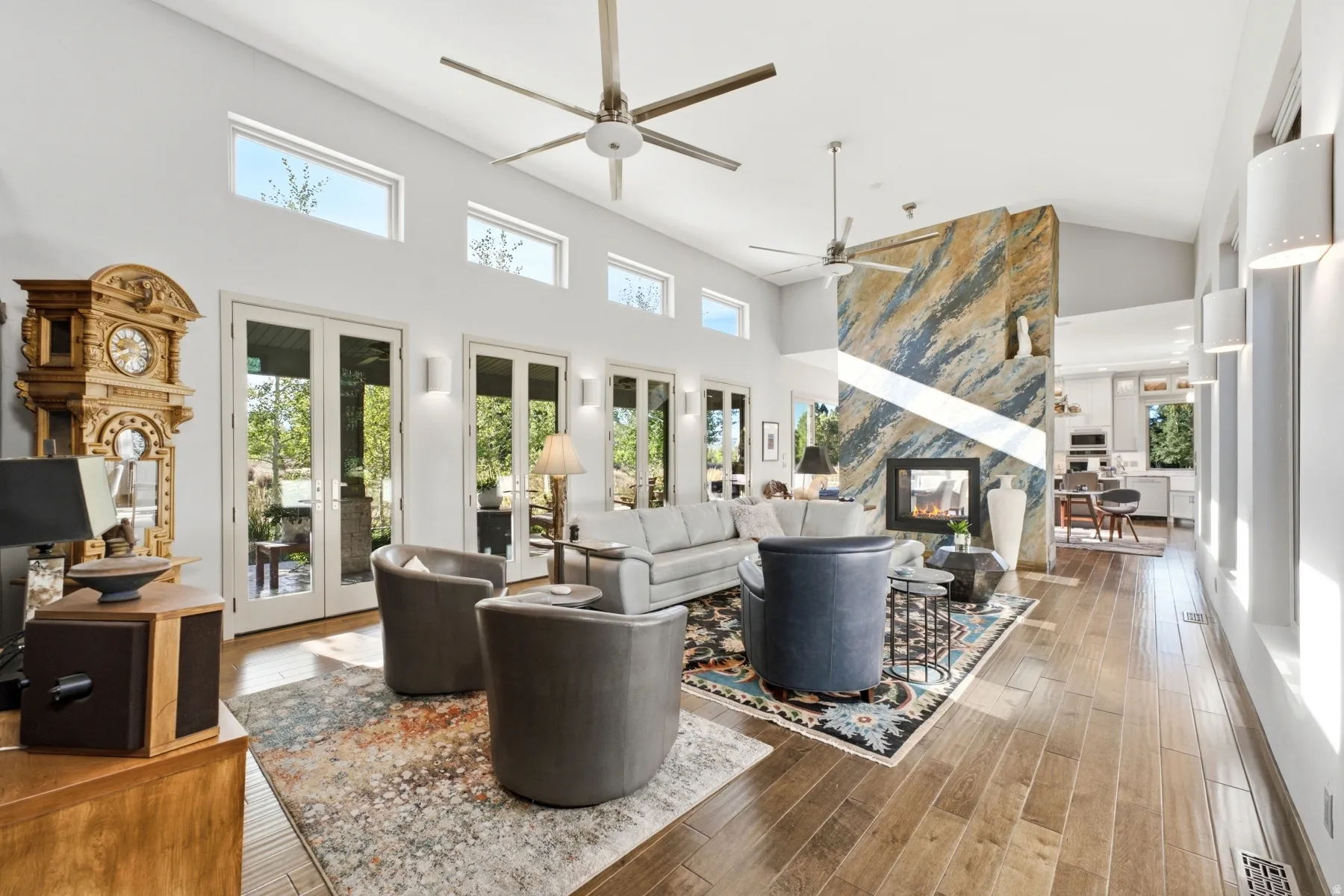 Vaulted ceiling with transom windows, wood-finish flooring, multiple French doors, and a fireplace with a stone-clad surround