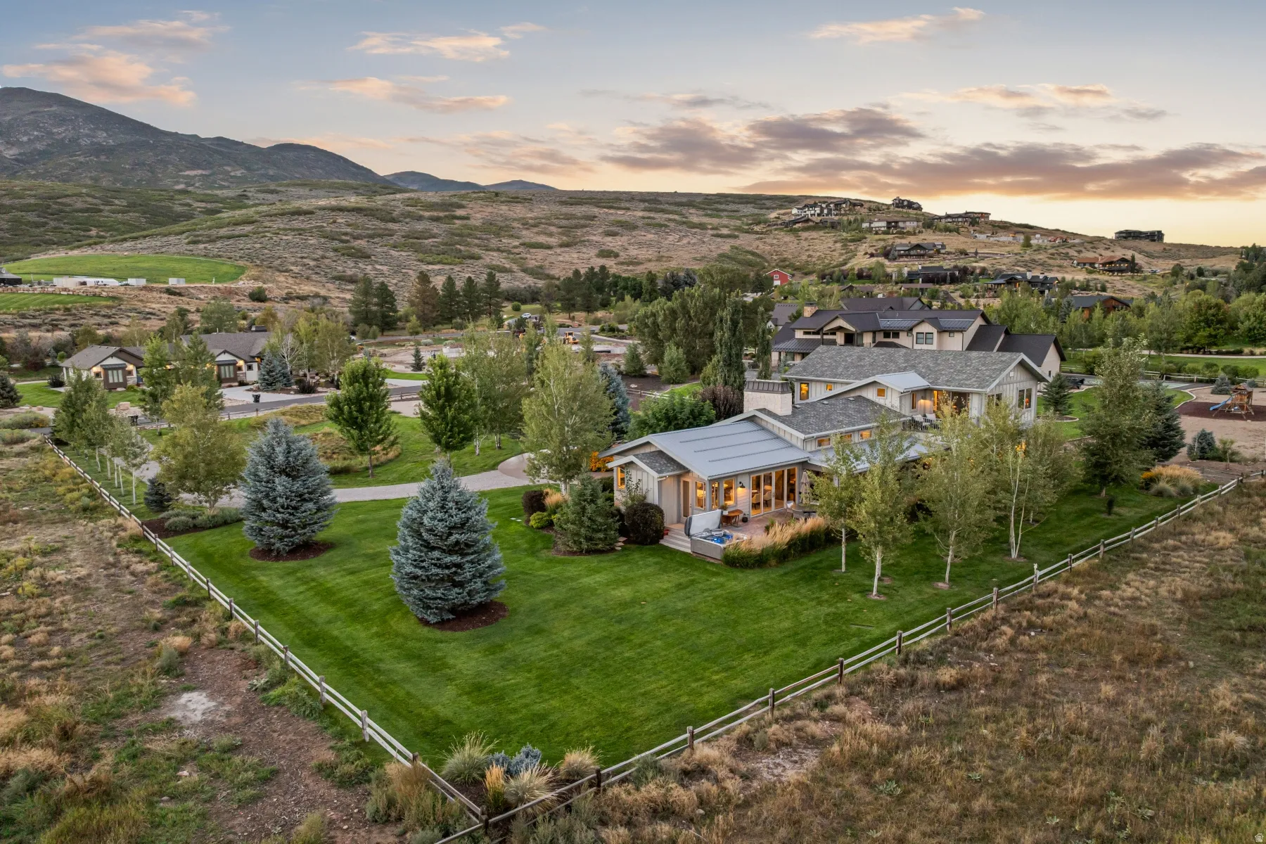 Expansive property featuring a well-maintained lawn, mature trees, mountain backdrop, and an outdoor patio with built-in spa