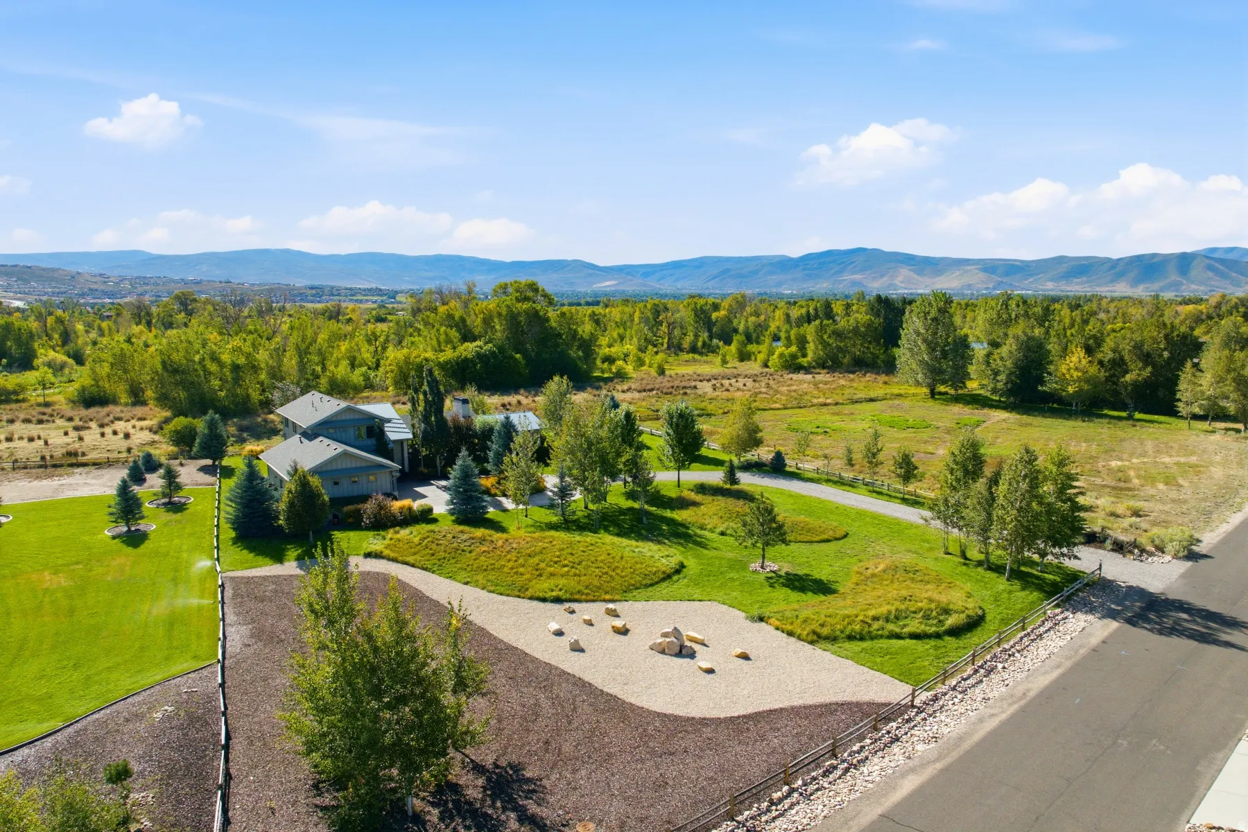 Expansive property featuring a residence with multiple gables, surrounding mature landscaping, and an extended gravel driveway
