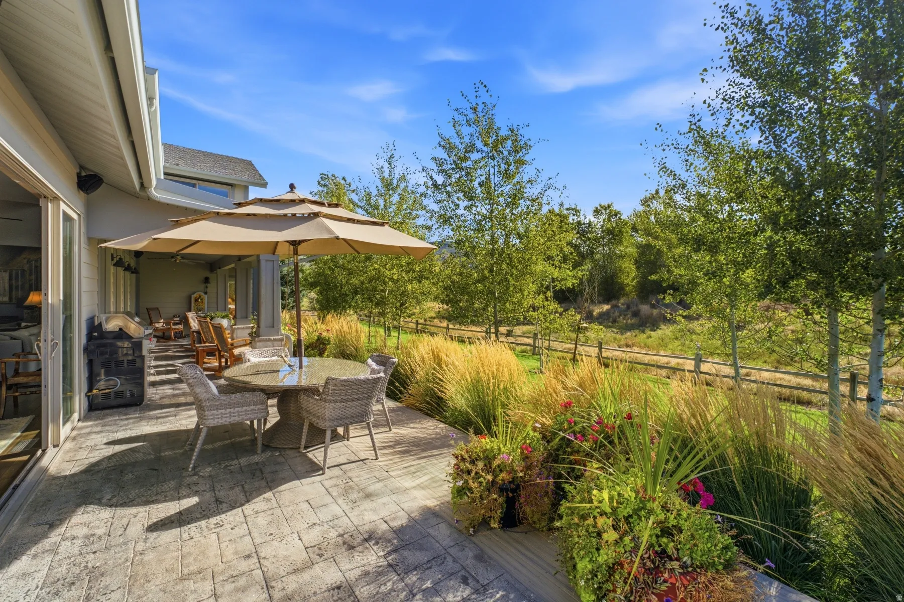 Stamped concrete patio, expansive covered outdoor area, mature perimeter trees, natural foliage, and a split rail fence