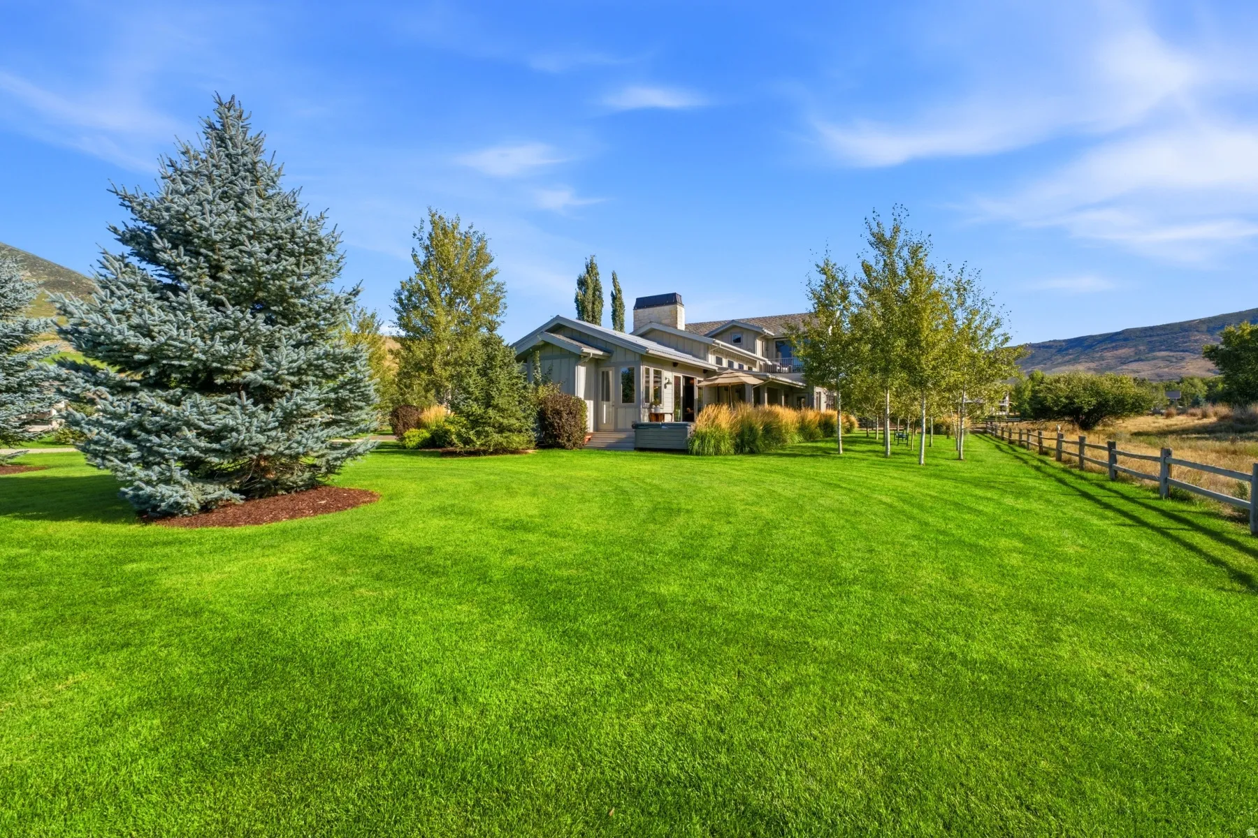Expansive green lawn, mature evergreen trees, and a multi-level residence with a prominent chimney