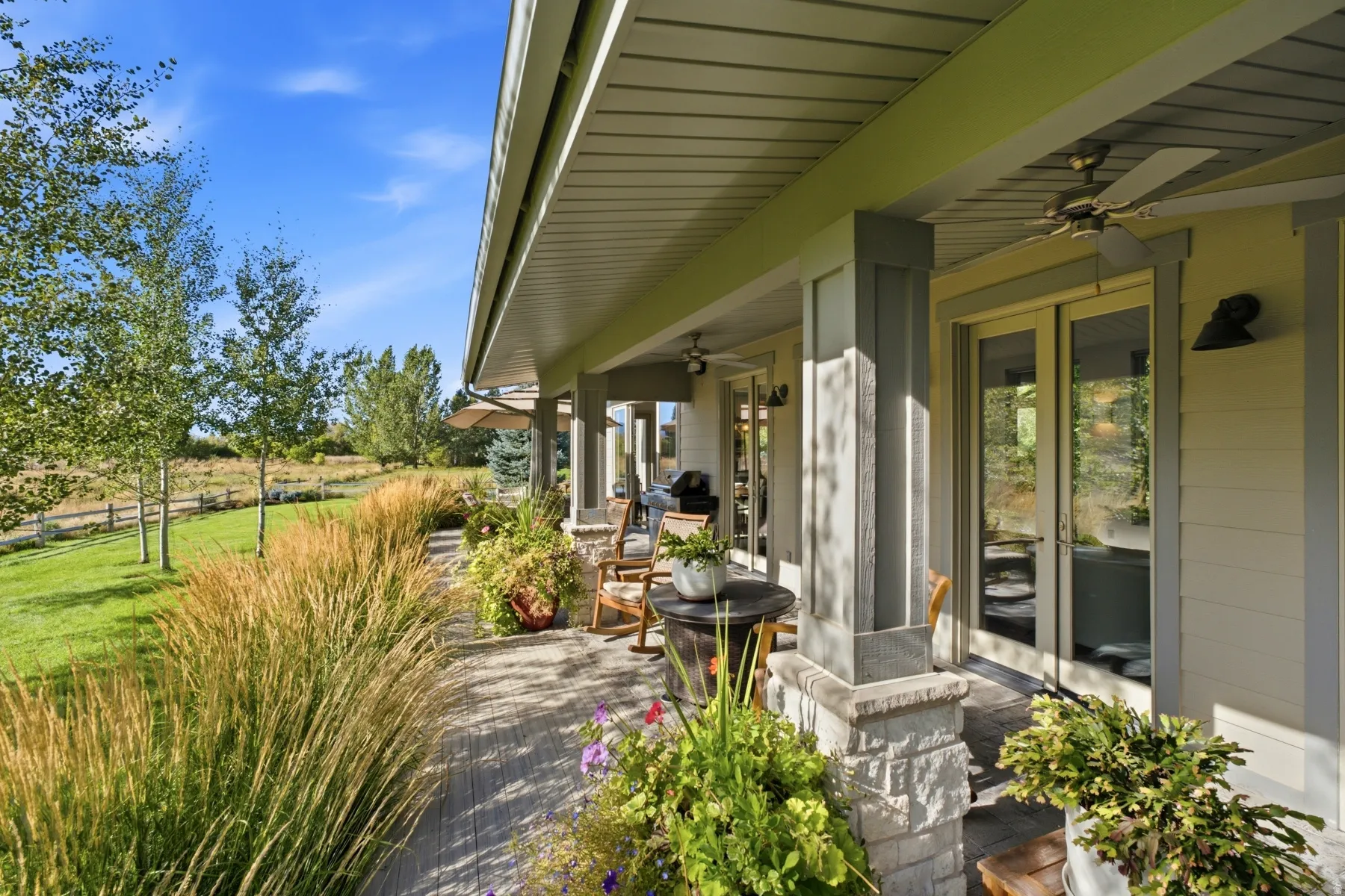 Expansive covered patio with stone-wrapped columns, double glass doors, and built-in ceiling fans