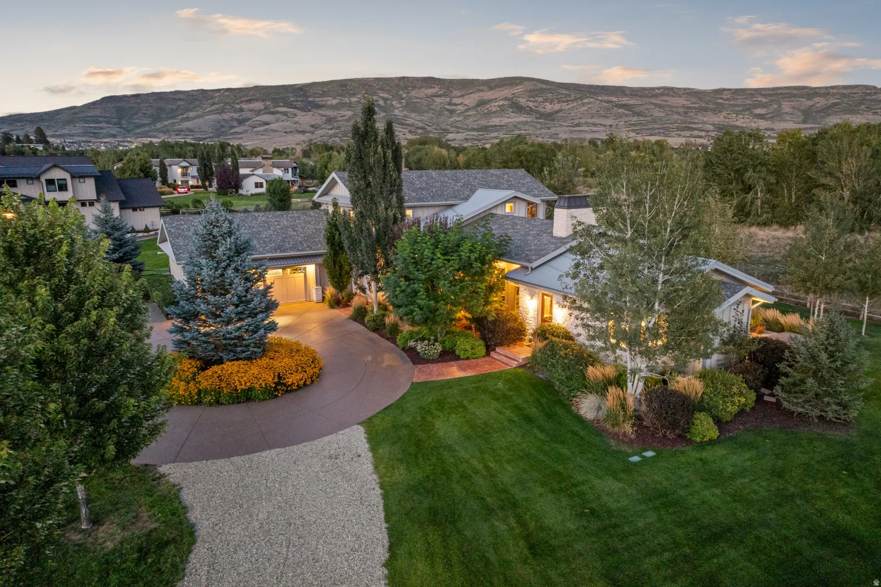 Expansive front yard with manicured lawn, established landscaping, and a curved driveway leading to an attached garage