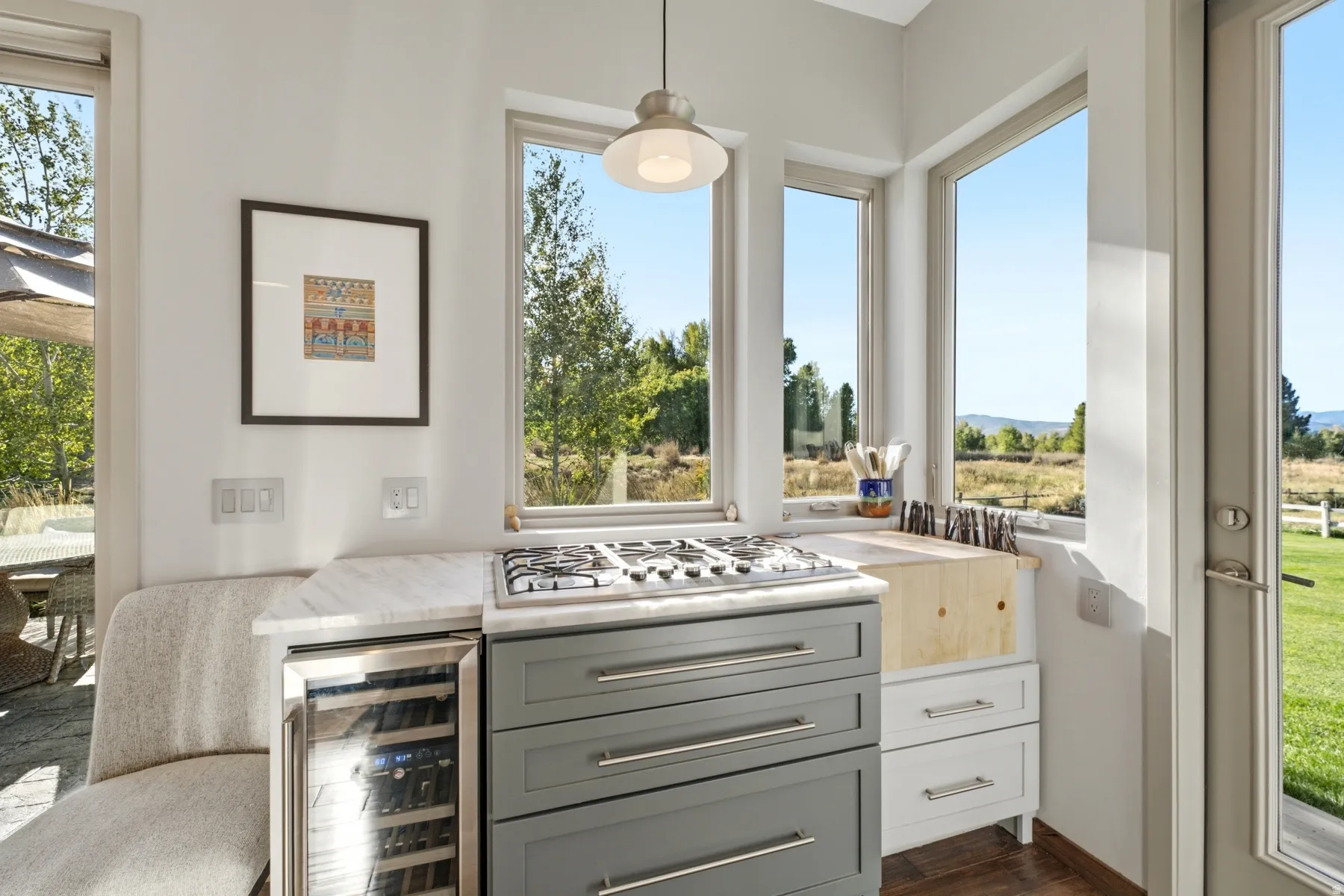 Built-in gas cooktop, integrated wine refrigerator, natural stone countertop, white shaker cabinetry, and multiple windows