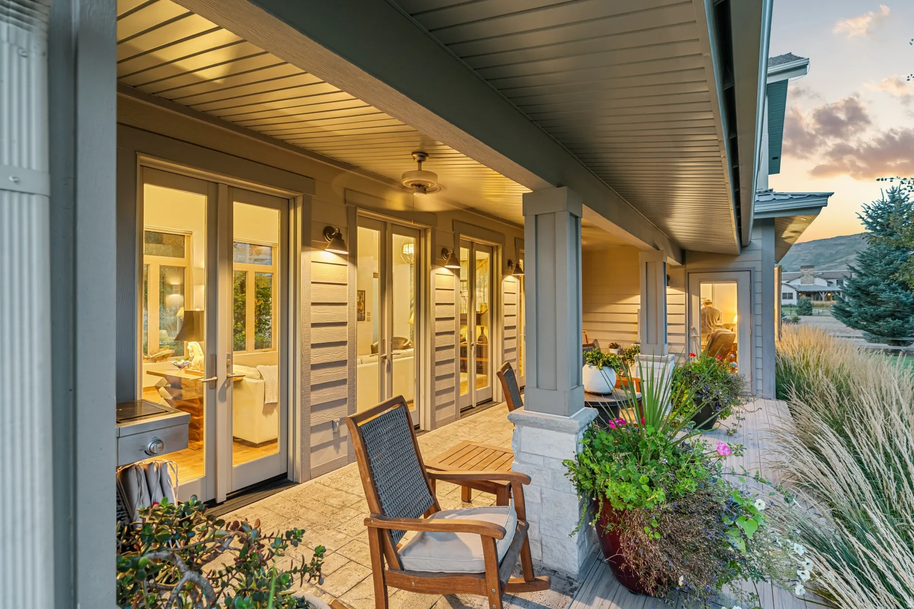 Covered patio with stone-wrapped columns, multiple sets of glass panel doors, and overhead lighting