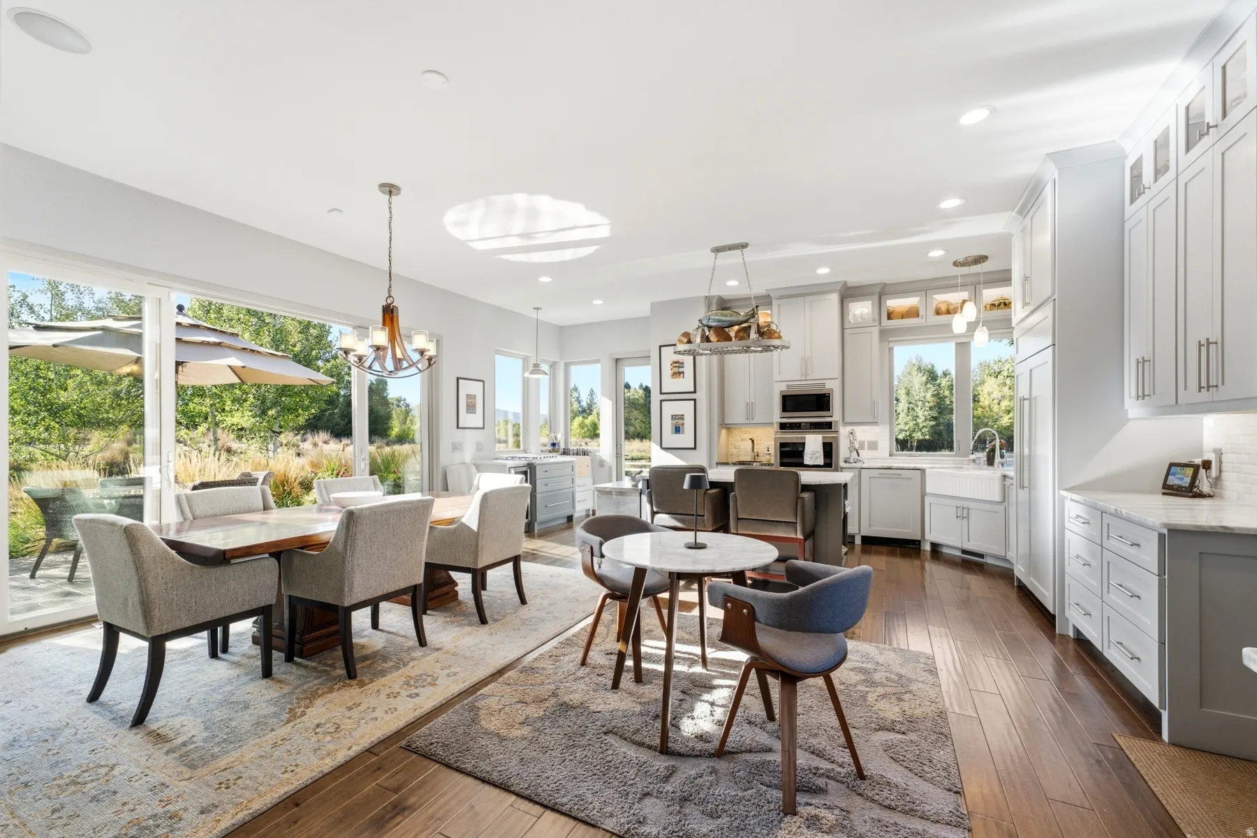 Expansive sliding glass doors, recessed ceiling lighting, wood-finish flooring, two-tone cabinetry, and a large farmhouse sink