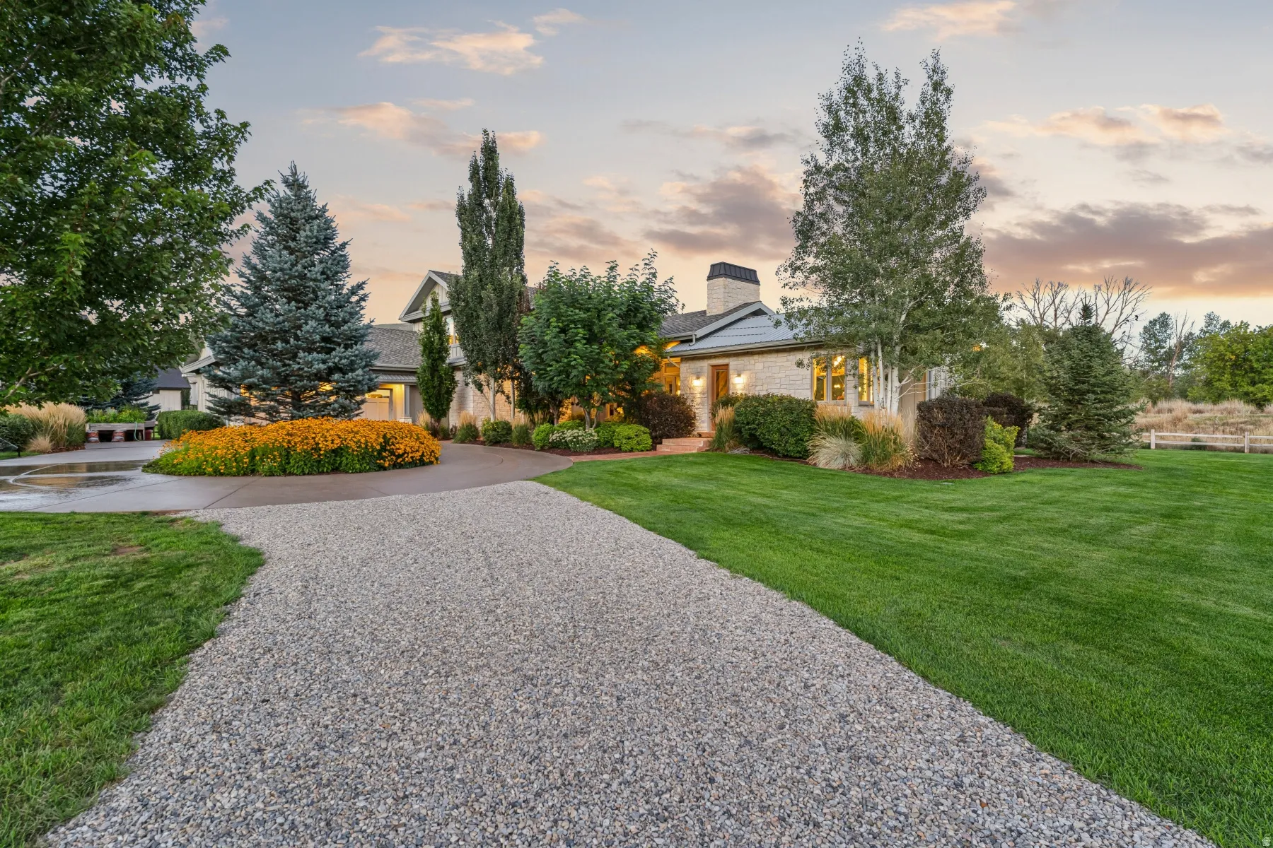 Expansive gravel driveway leading to a circular concrete drive, flanked by a manicured lawn and mature landscaping
