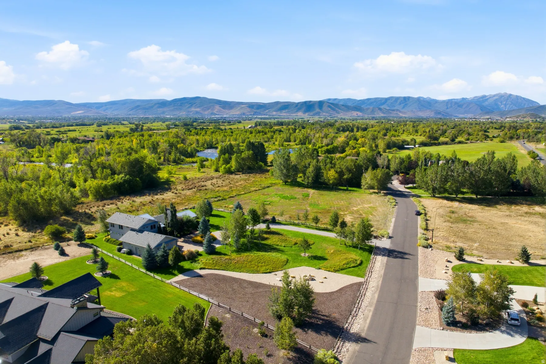 Expansive property with a paved road, mature trees, green lawns, and a mountainous backdrop
