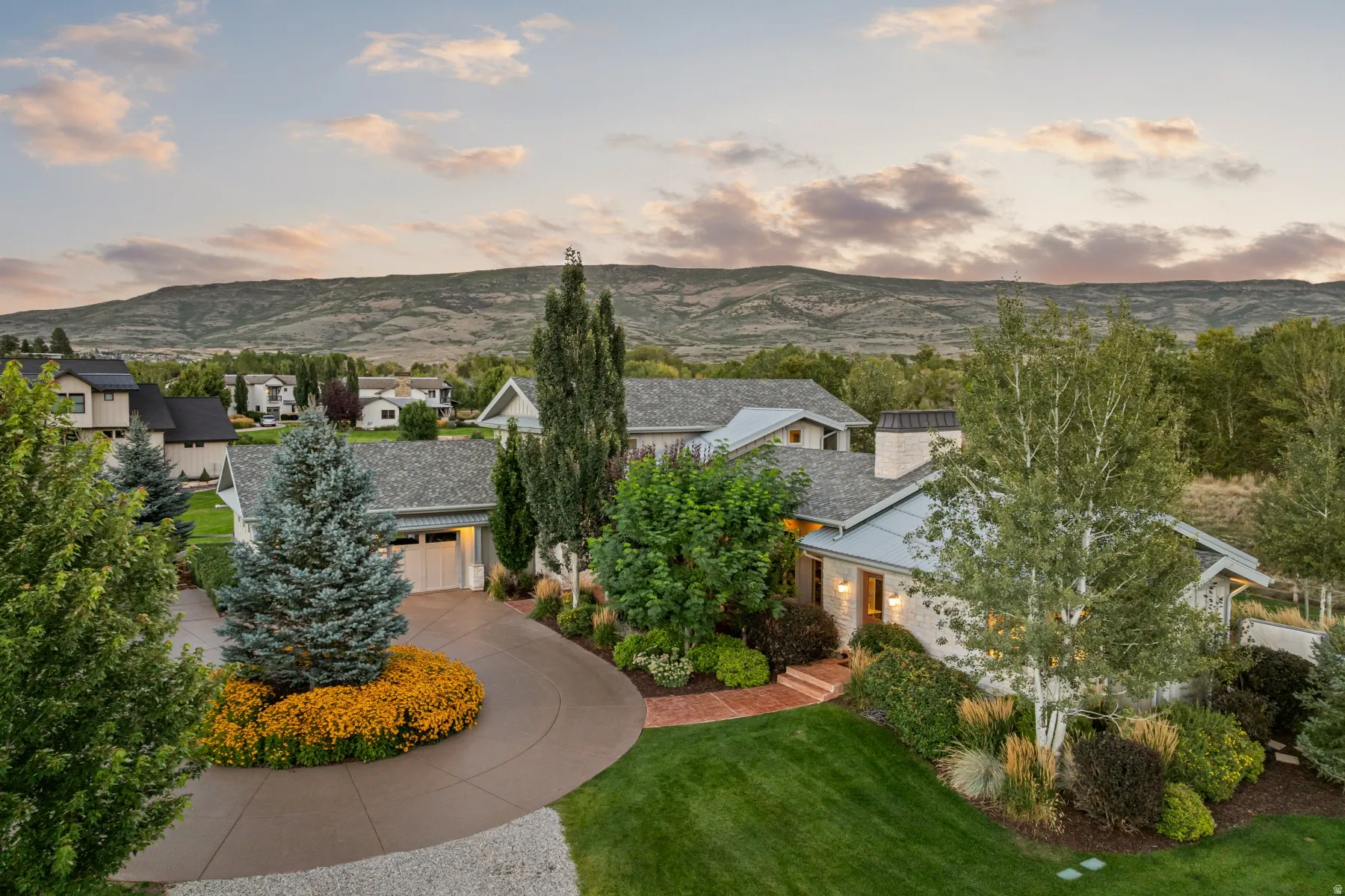 Expansive property featuring a circular driveway, mature landscaping, integrated garage, and mountain backdrop