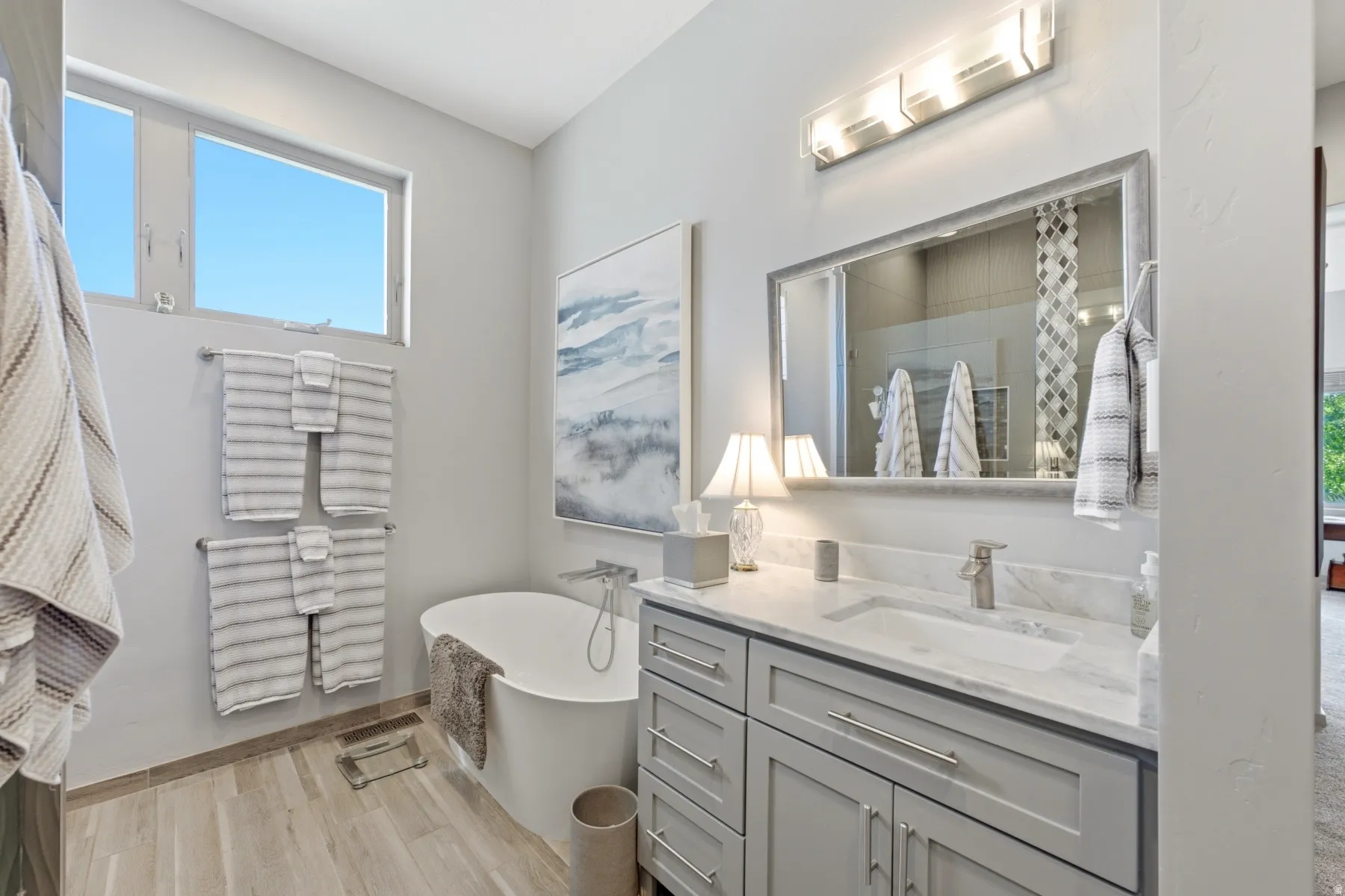 Freestanding soaking tub, wood-finish flooring, dual-pane windows, single vanity with integrated sink, and contemporary light fixtures