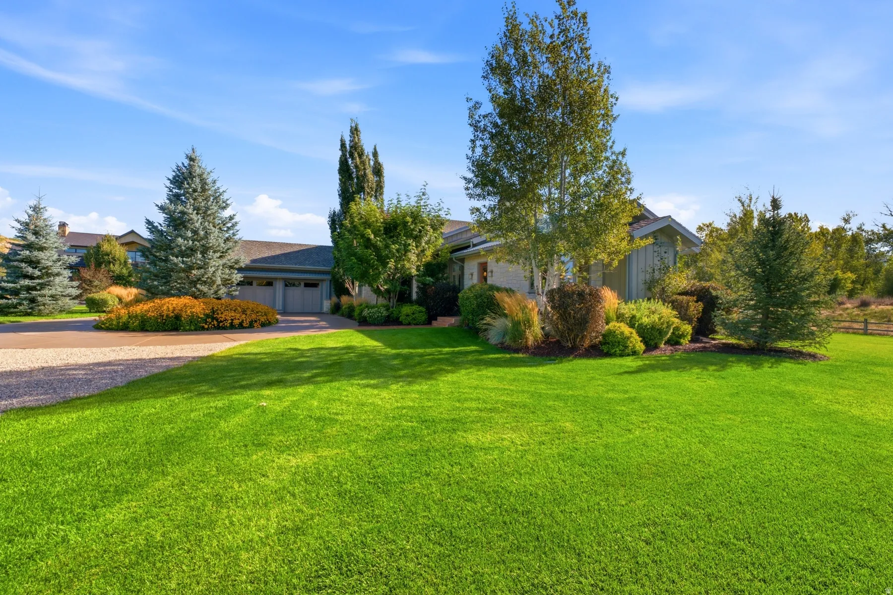 Expansive front lawn with mature trees, gravel driveway, and integrated two-car garage