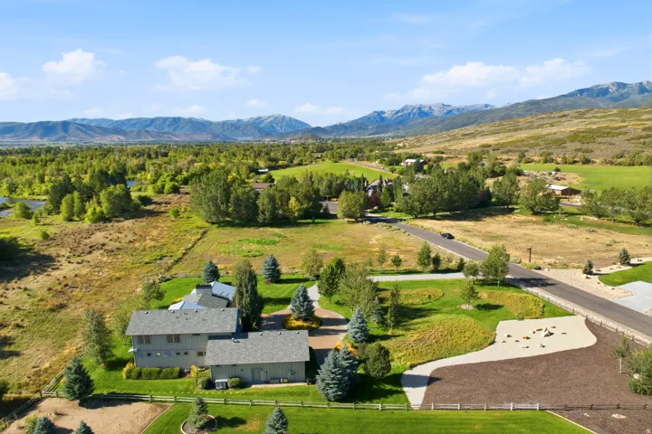 Expansive property featuring a multi-level residence, detached garage structure, paved driveway, and manicured lawns, all set against a backdrop of distant mountains
