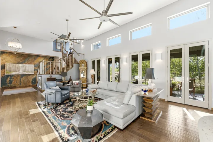 Vaulted ceilings with contemporary ceiling fans, wood-finish flooring, multiple sets of glass-paned French doors, a prominent staircase with wood railing, and a feature wall with stone-finish paneling