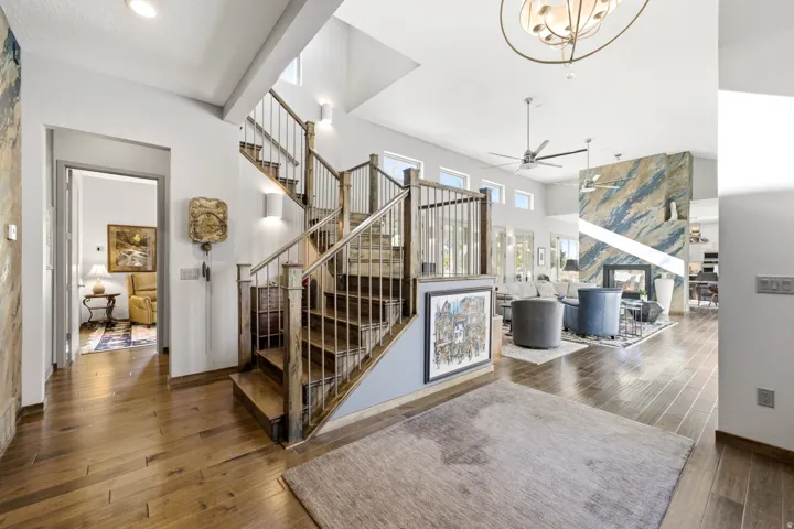 Expansive open-concept living space with wood-finish flooring, a contemporary floating staircase with metal balusters, high ceilings, and a fireplace with a striking accent wall