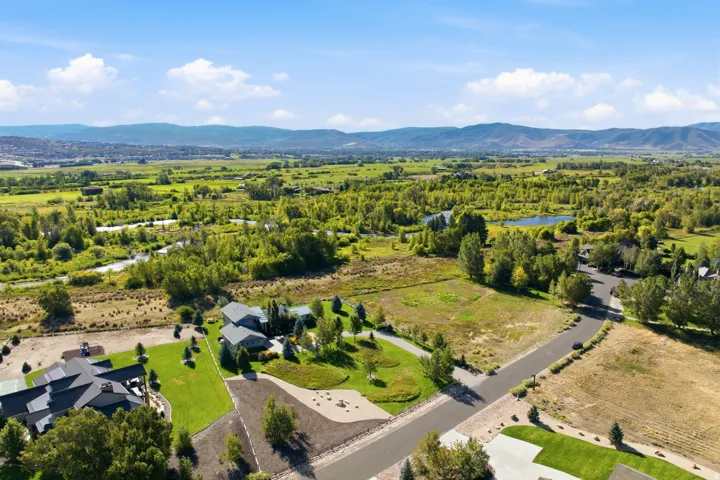 Expansive landscape featuring distant mountains, lush green fields, mature trees, and a visible waterway