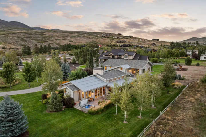 Expansive estate featuring a stucco and siding exterior, multiple gabled roofs, a paved patio with a hot tub, a large manicured lawn, and mature trees