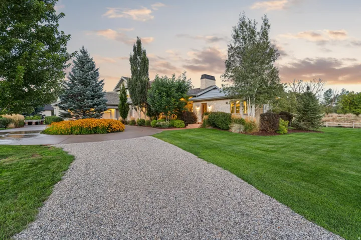 Expansive gravel driveway leading to a circular concrete drive, flanked by a manicured lawn and mature landscaping