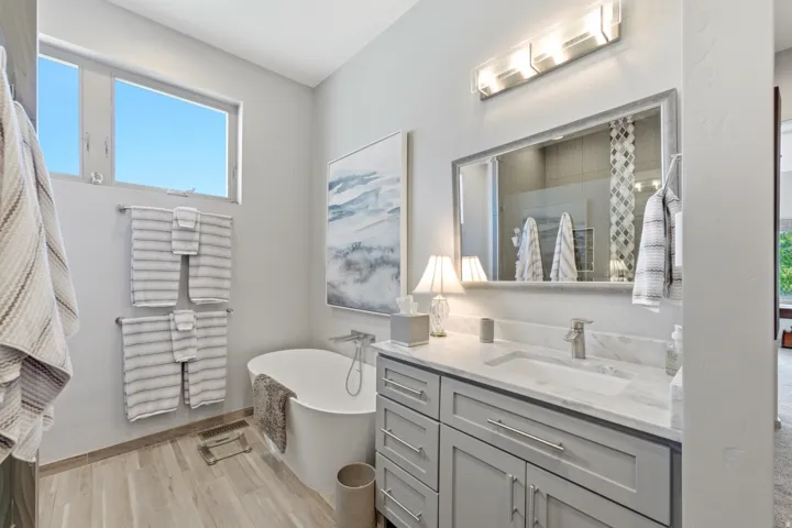 Freestanding soaking tub, wood-finish flooring, dual-pane windows, single vanity with integrated sink, and contemporary light fixtures