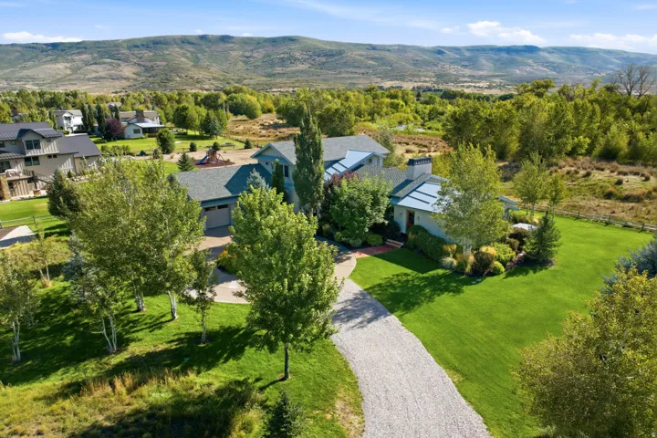 Expansive gravel driveway leading to a two-car garage, surrounded by mature trees and manicured lawns