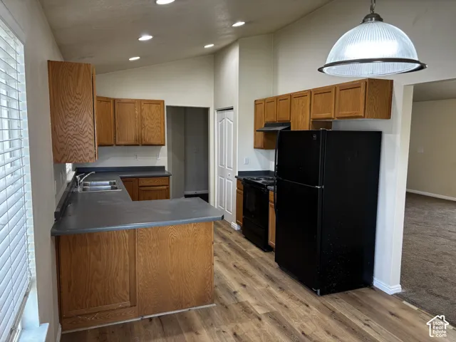 Kitchen featuring wood-finish cabinetry, dark countertops, a double basin sink, recessed lighting, and wood-finish flooring