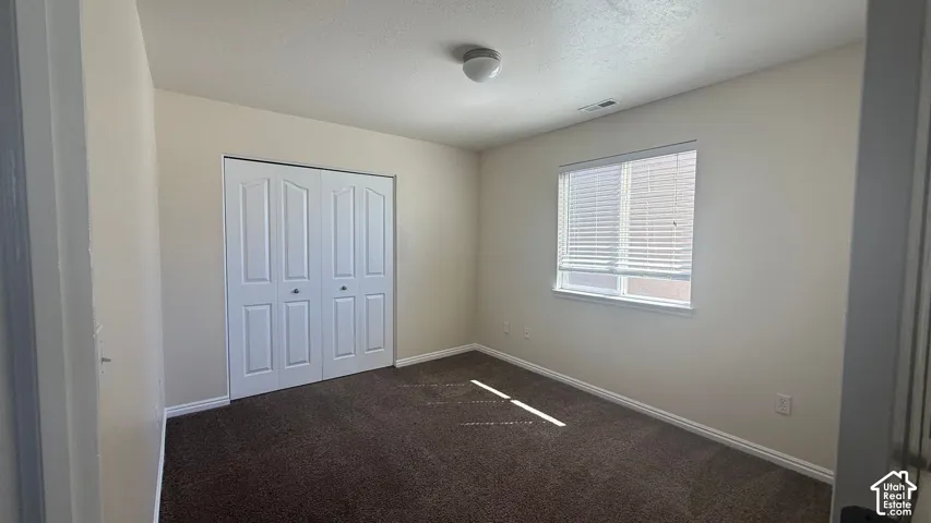 Neutral-toned wall paint, carpet flooring, a window with horizontal blinds, and a bi-fold closet door