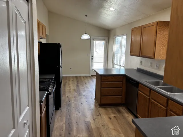 Kitchen featuring wood-finish flooring, wood cabinetry, dark countertops, and a vaulted ceiling