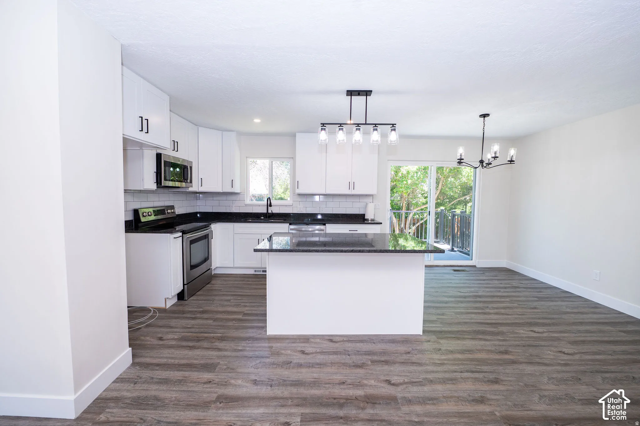 White kitchen cabinetry with dark countertops, stainless steel appliances, and wood-finish flooring