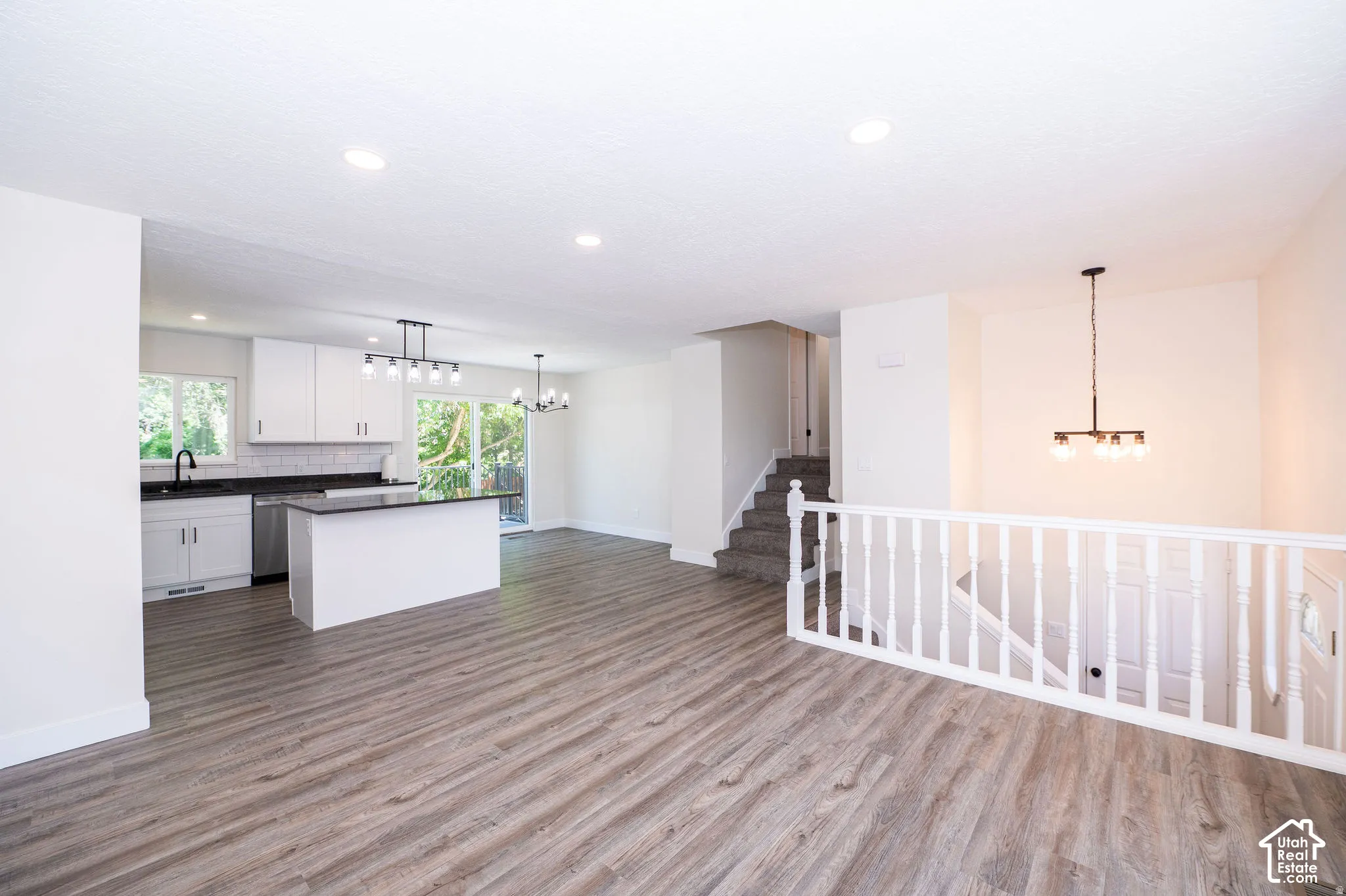 Open-concept living space featuring wood-finish flooring, white kitchen cabinetry with dark countertops, a kitchen island, and contemporary lighting fixtures