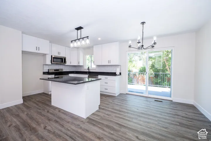 Modern kitchen featuring white cabinetry, dark countertops, subway tile backsplash, stainless steel microwave, and wood-finish flooring