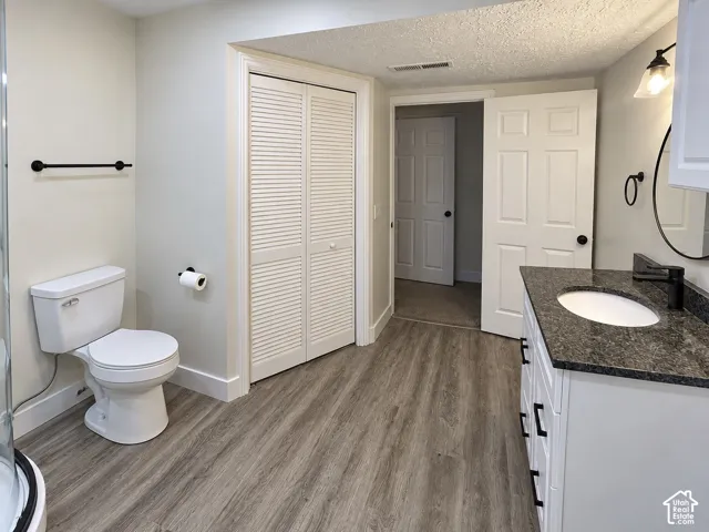 Bathroom featuring wood-finish flooring, a white vanity with a dark stone countertop, an oval wall-mounted mirror, matte black hardware, and louvered closet doors