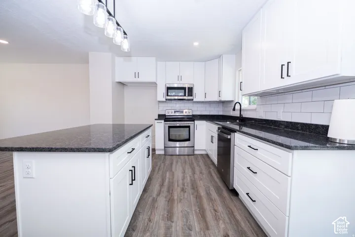 Kitchen featuring a large island, dark countertops, white cabinetry, stainless steel appliances, and wood-finish flooring