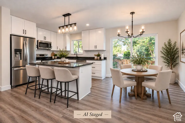 Kitchen featuring white shaker-style cabinetry, dark stone countertops, stainless steel appliances, wood-finish flooring, and dual hanging chandeliers