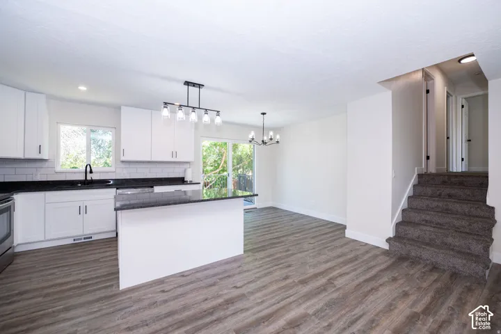 White cabinetry with black countertops, a subway tile backsplash, a kitchen island, and wood-finish flooring
