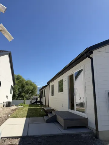 Sliding glass door opening to an elevated deck with composite decking, featuring three steps down to a concrete patio and a newly seeded lawn area
