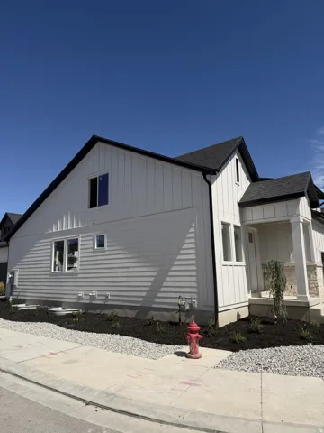 Contemporary exterior with white vertical and horizontal siding, dark roof, dark gutters, and stone accent column
