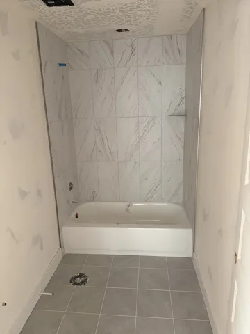 White soaking tub with integrated shelving, surrounded by large format tile with subtle veining
